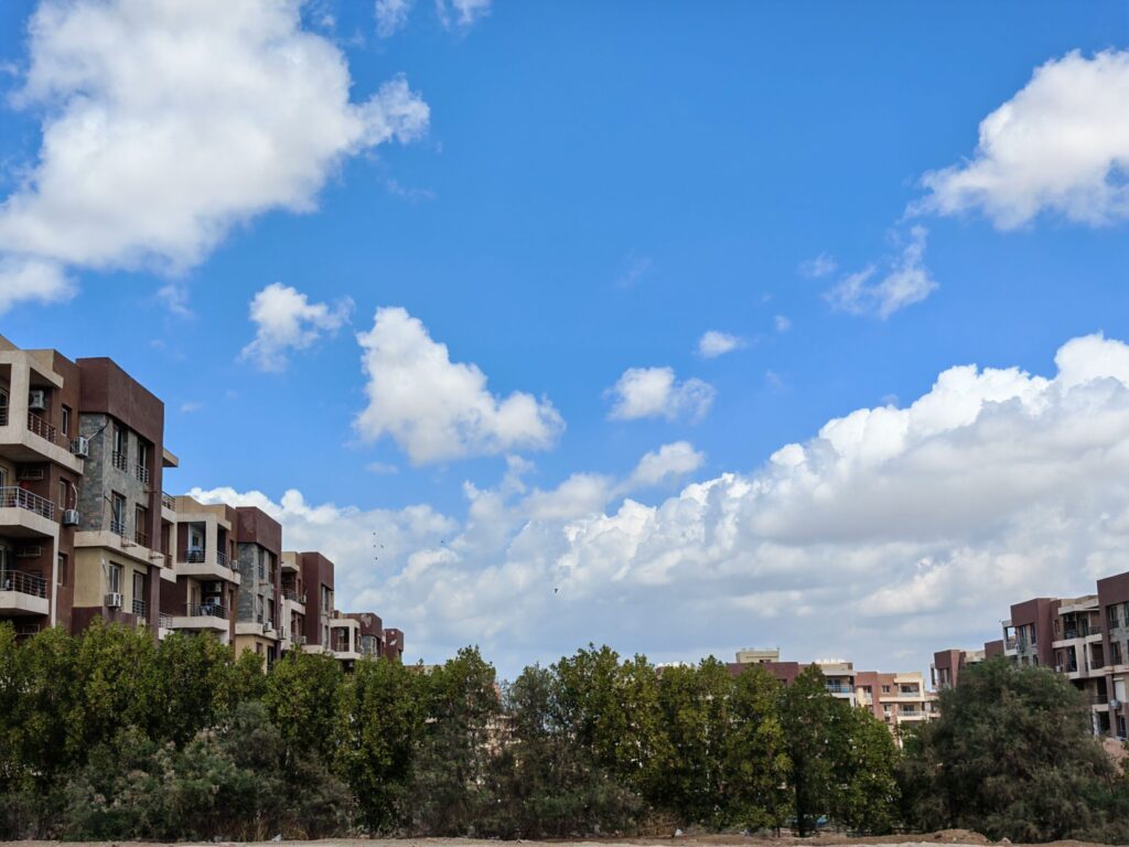 Low-rise cream and terracotta apartment buildings with landscaped greenery under a blue sky in Dubai