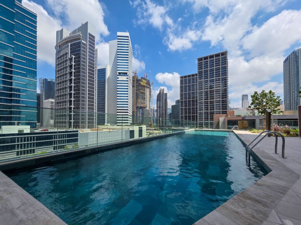 Rooftop swimming pool with glass-fronted high-rise towers under a blue sky, similar to the rooftop pool at Sevanam Crown, Dubai Silicon Oasis