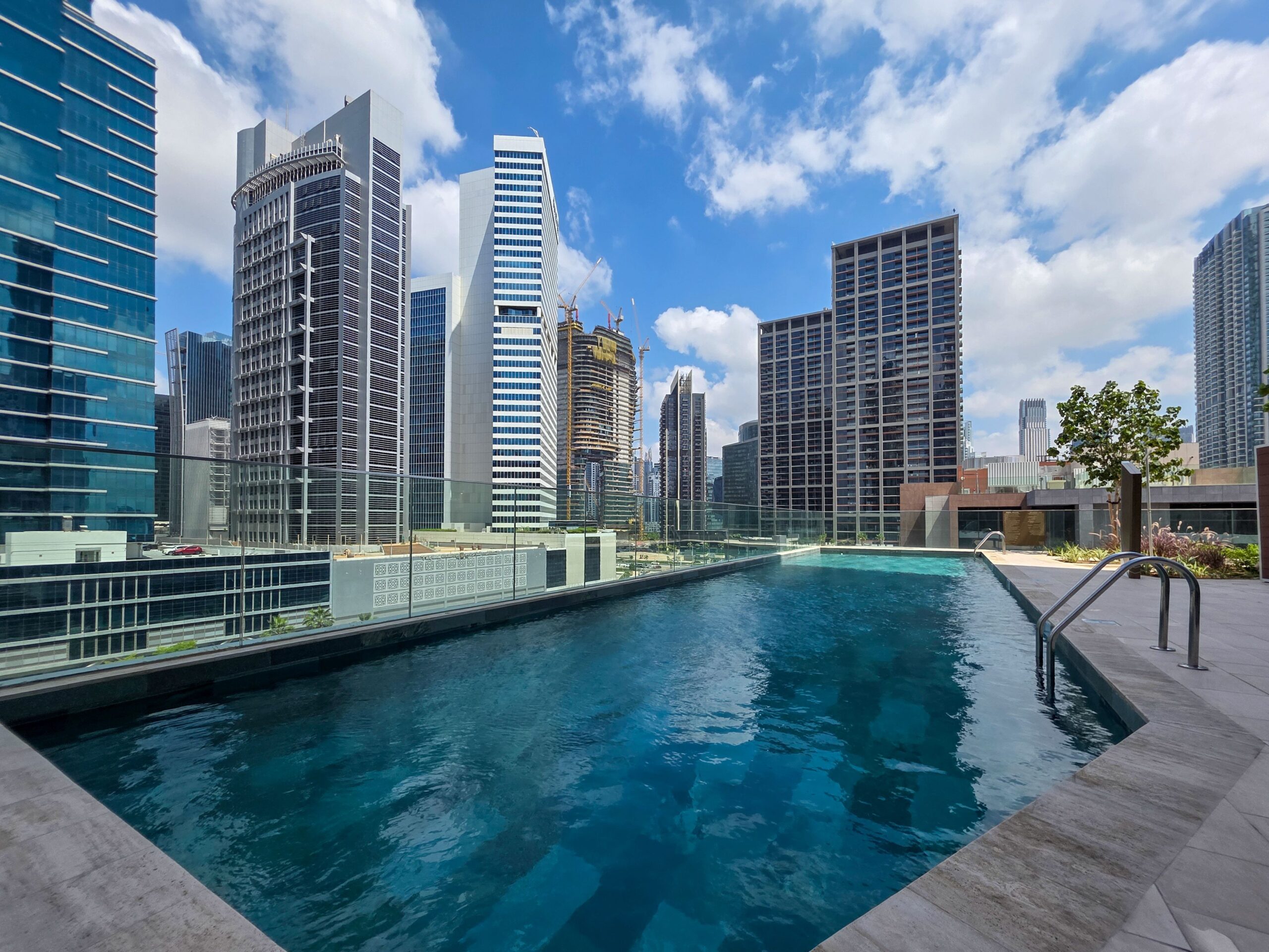 Rooftop swimming pool with glass-fronted high-rise towers under a blue sky, similar to the rooftop pool at Sevanam Crown, Dubai Silicon Oasis