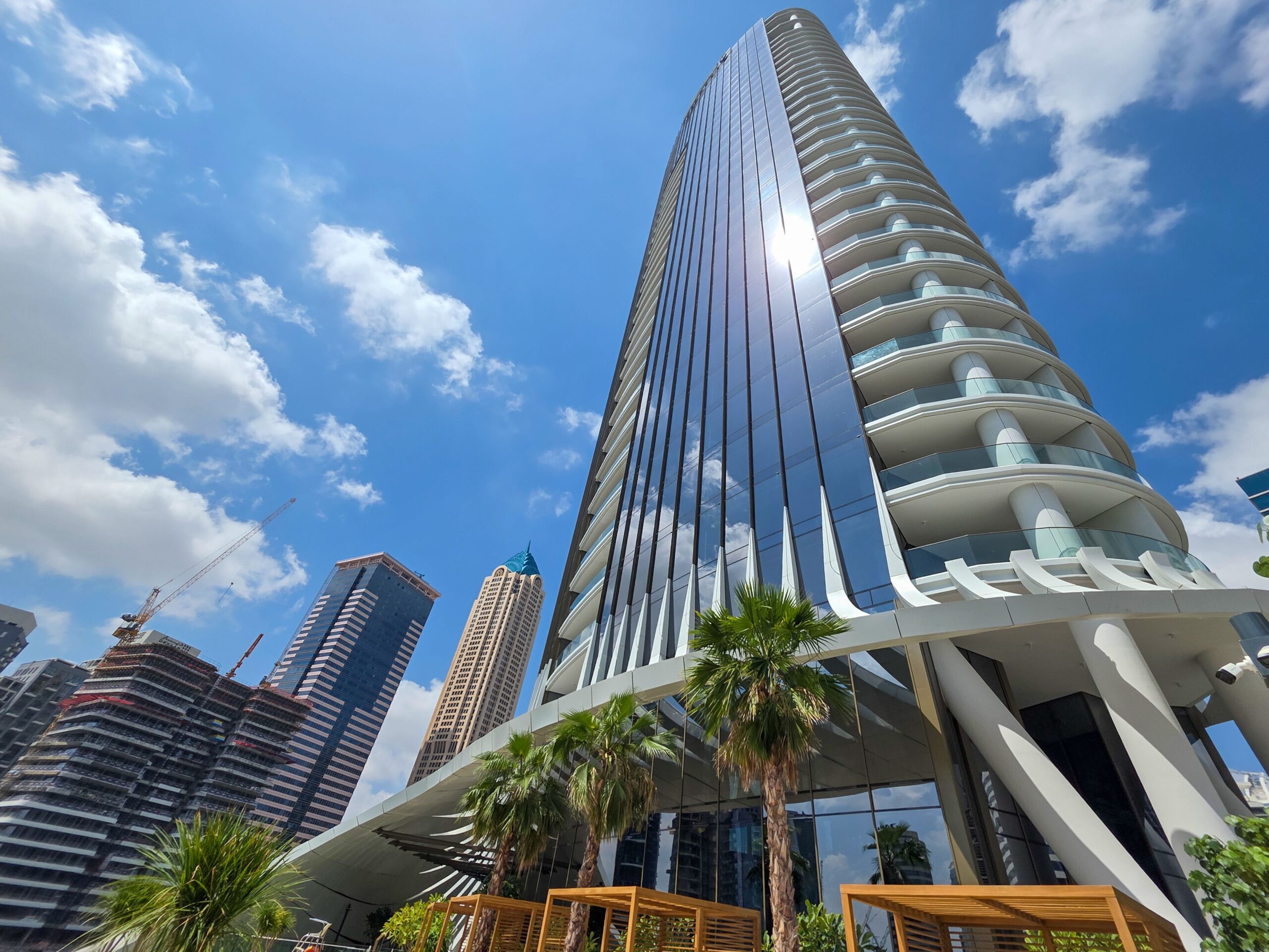 Modern glass residential tower with curved balconies and palm trees under a blue sky in Dubai