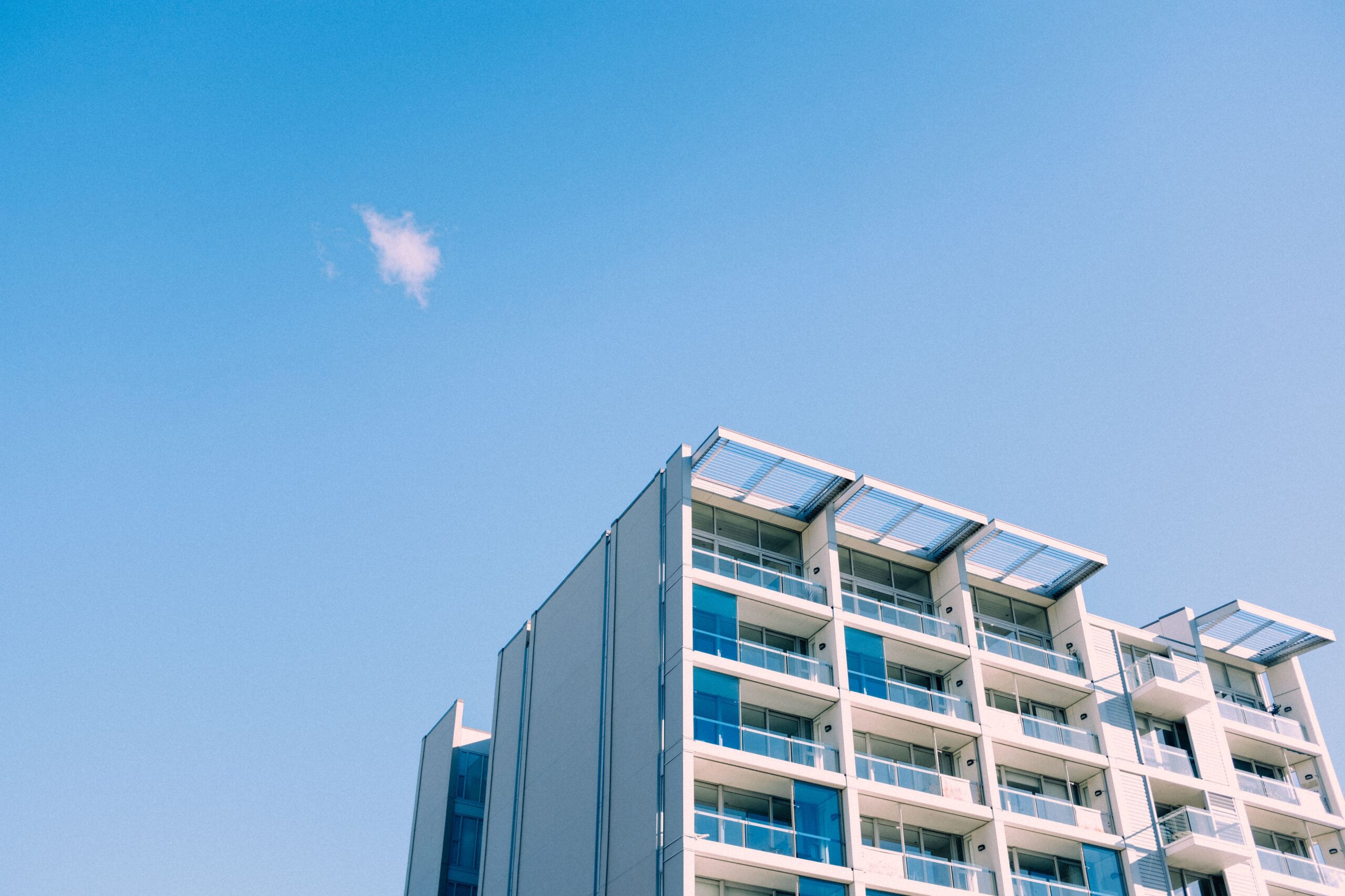 Modern apartment building corner with glass balconies and shade awnings under a clear blue sky, representative of Binghatti Vista in Dubai Silicon Oasis, Dubai