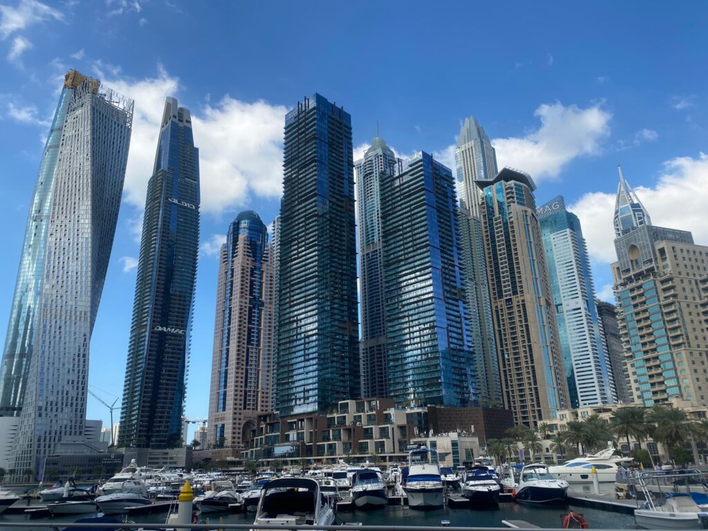 Glass residential skyscrapers above a marina with moored boats under a bright blue sky