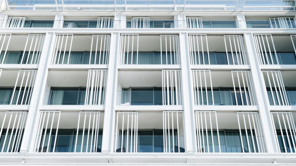 Close-up of a modern white apartment building facade with vertical louvre balcony screens and blue-tinted glass windows, evocative of a Liwan, Dubai residential development