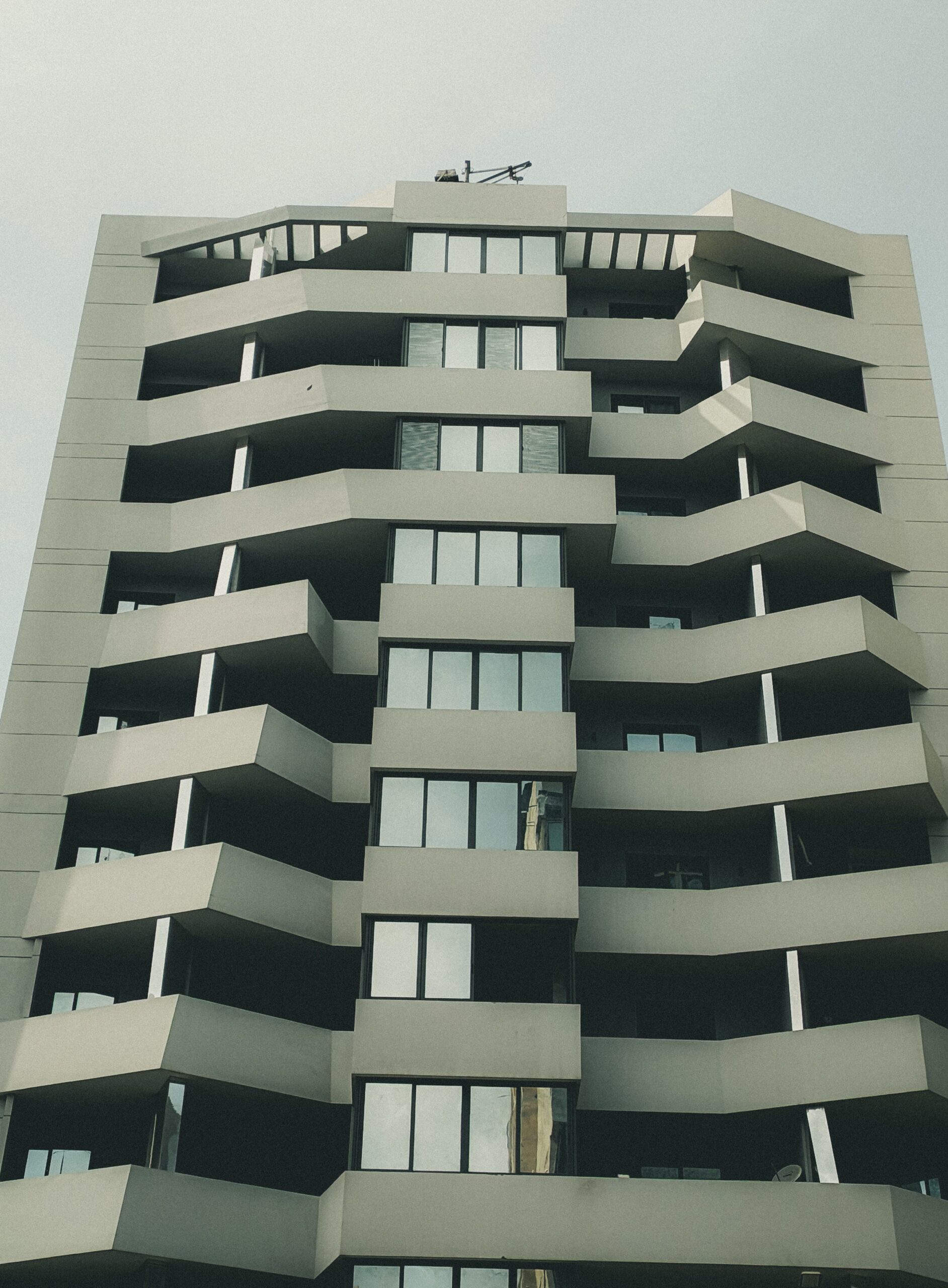 Low-angle view of a modern Dubai apartment tower with zigzag balconies under an overcast sky