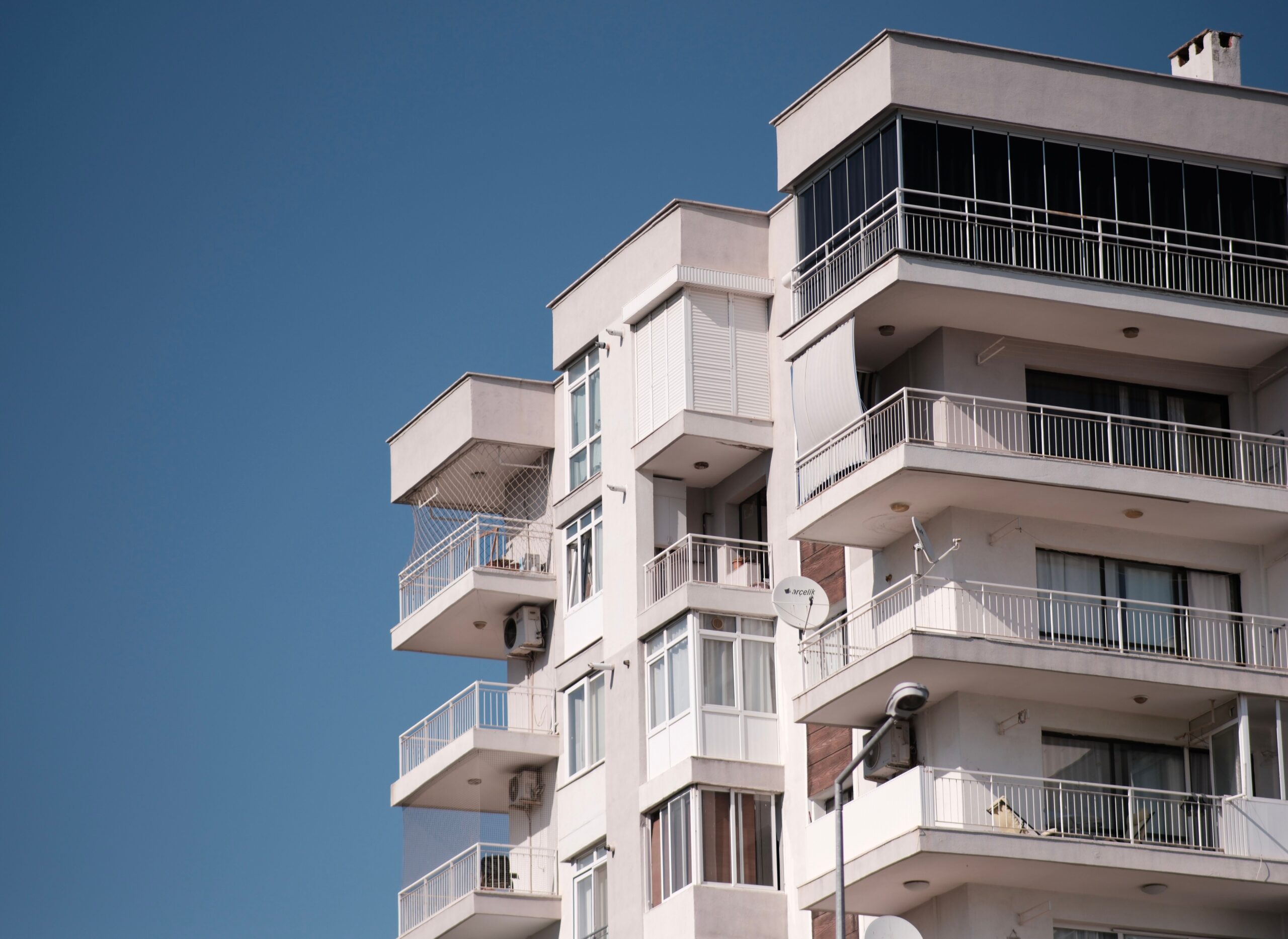 Cream and white mid-rise apartment building with stepped balconies under a clear blue sky, similar in style to Croesus Building, Majan