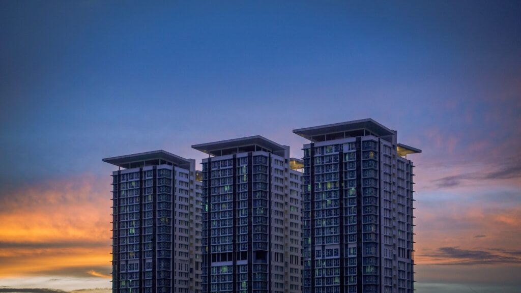 Three modern residential towers against a blue and orange sunset sky, near Wimbledon Tower, Dubai Sports City