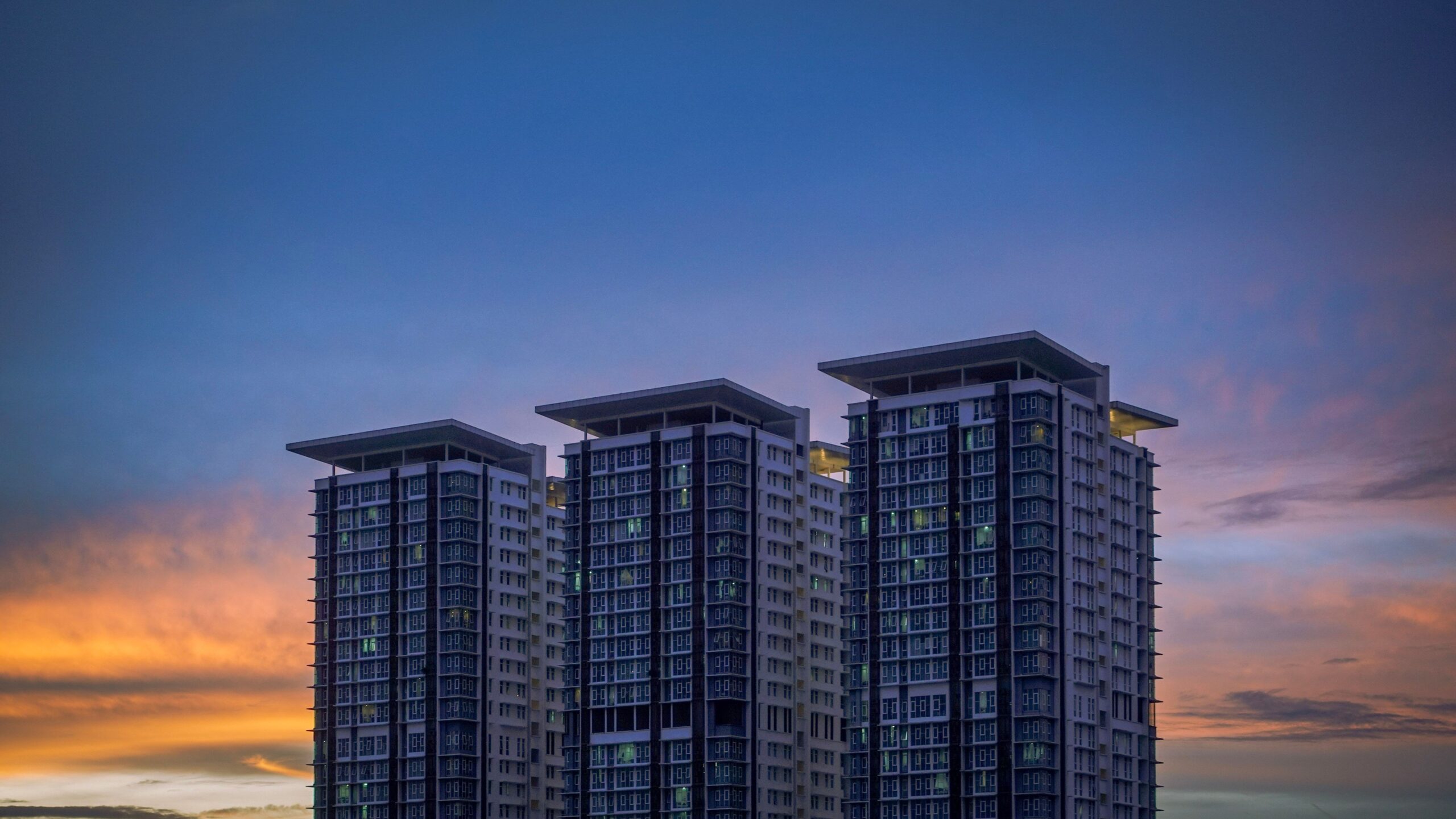 Three modern residential towers against a blue and orange sunset sky, near Wimbledon Tower, Dubai Sports City