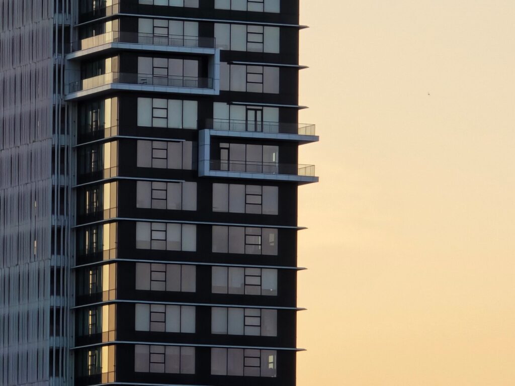 Close-up corner view of a modern high-rise apartment tower with balconies at sunset, representative of Topaz Avenue in Al Furjan, Dubai