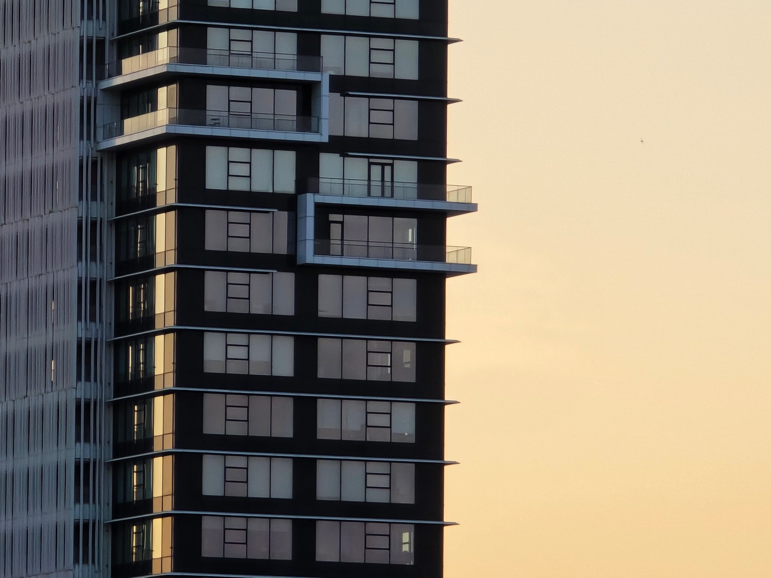 Close-up corner view of a modern high-rise apartment tower with balconies at sunset, representative of Topaz Avenue in Al Furjan, Dubai