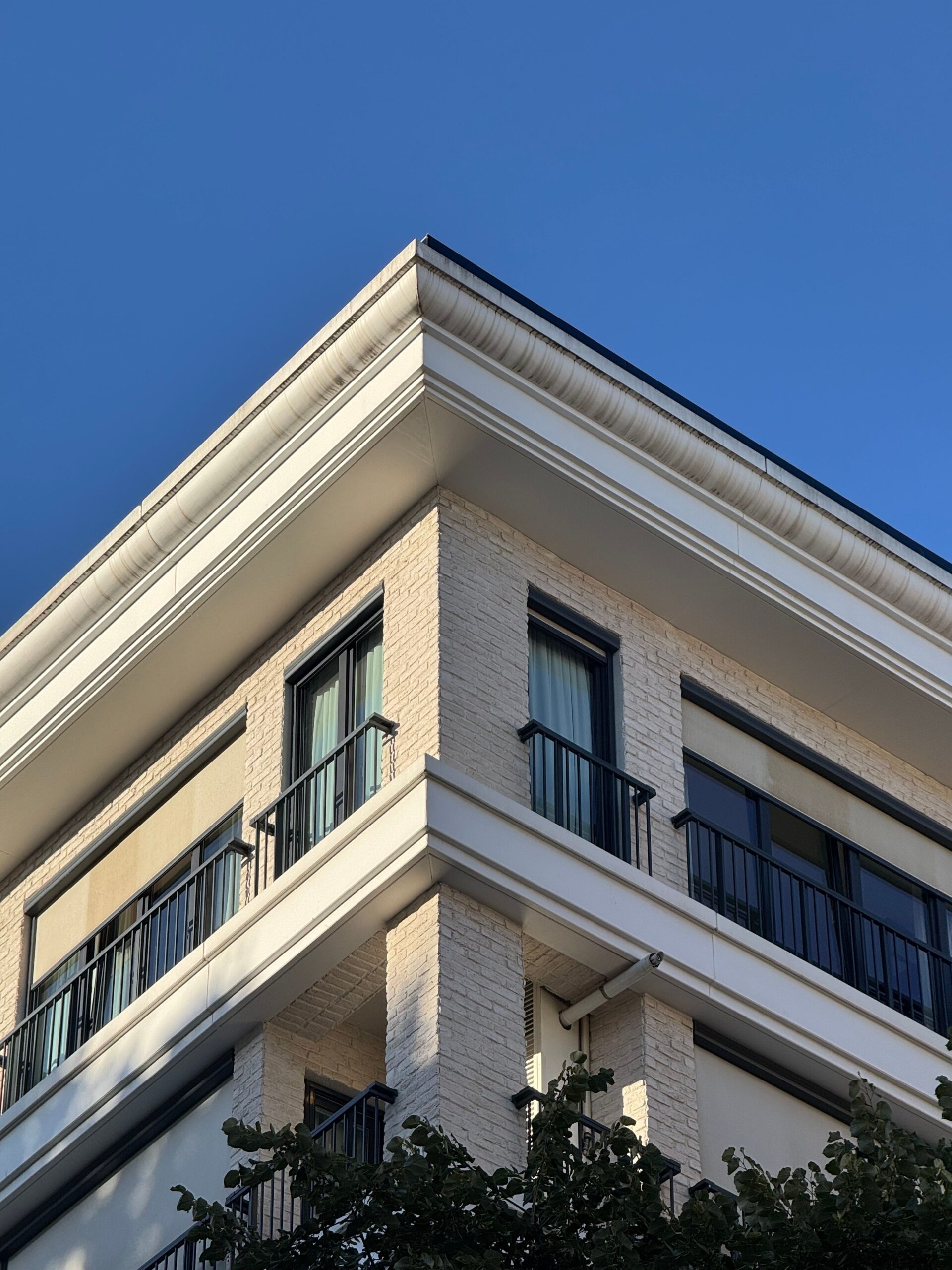 Corner of a cream mid-rise apartment building with balconies against a clear blue sky in Dubai