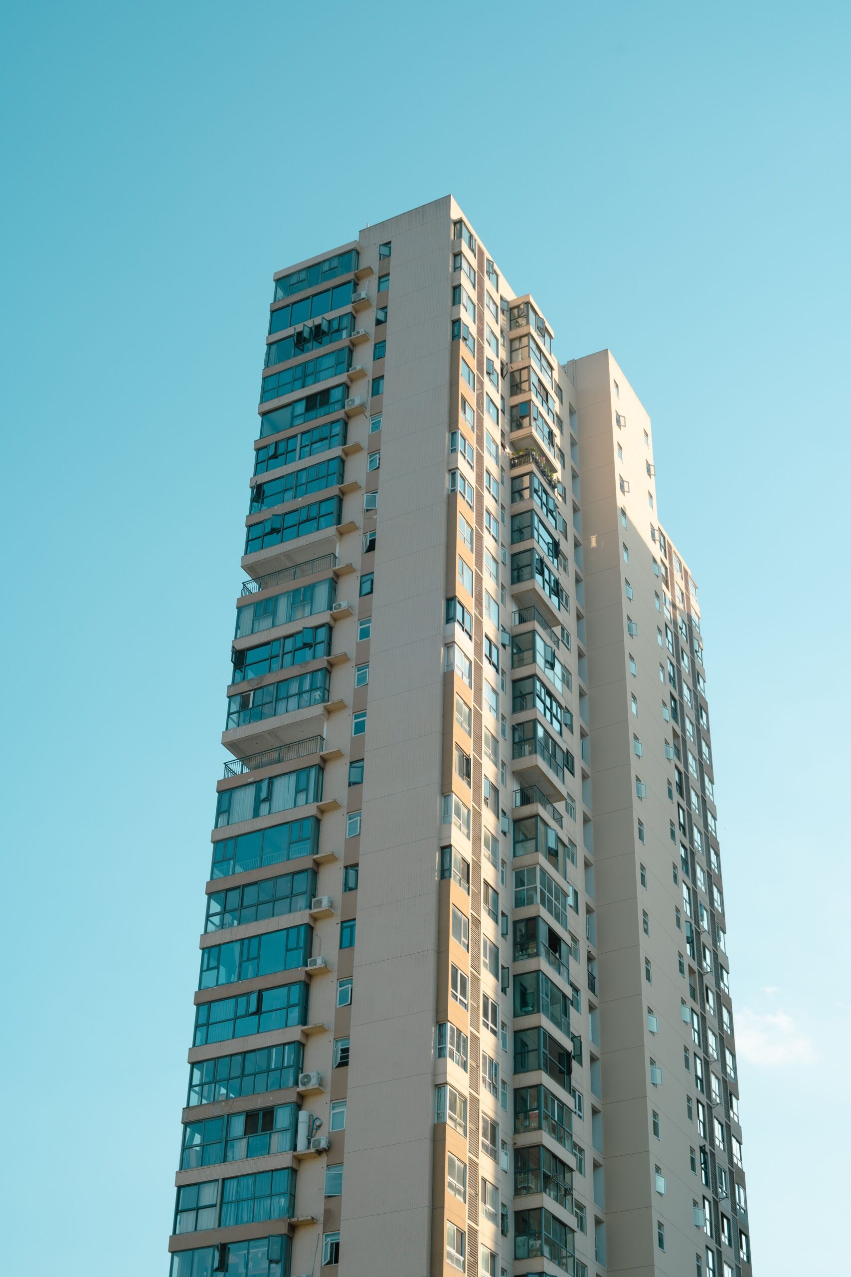 Cream-toned high-rise apartment building with balconies under a clear blue sky, representative of Binghatti Pearls in Dubai Silicon Oasis, Dubai