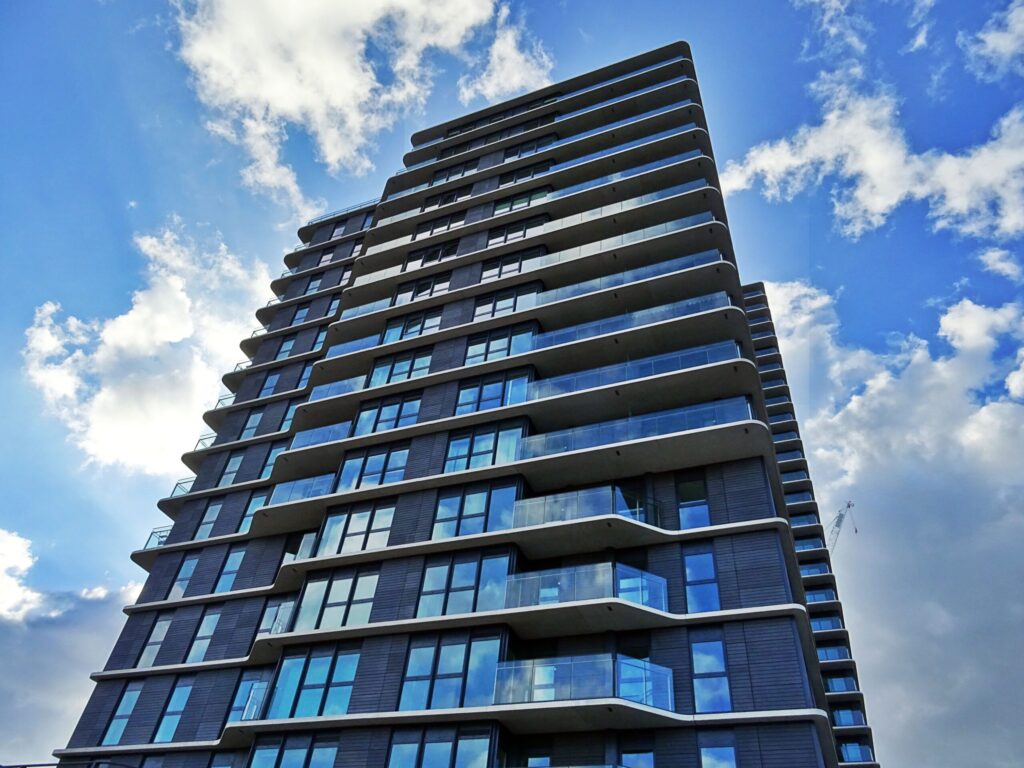 Glass-fronted apartment tower with balconies rising into a partly cloudy sky