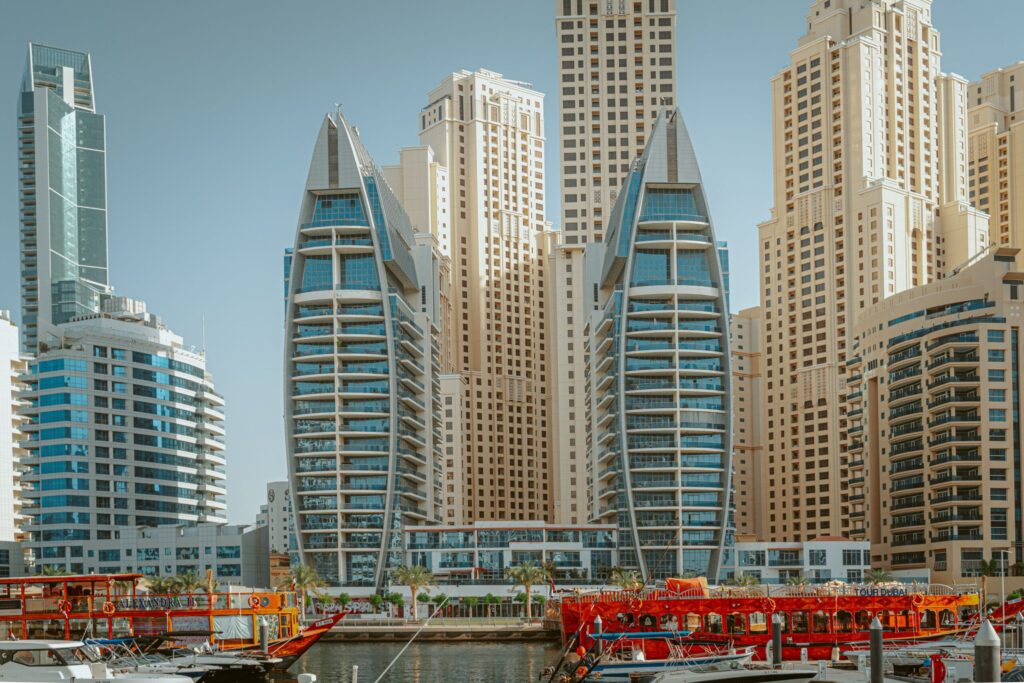 Dubai Marina's sail-shaped twin towers viewed from the water near Murjan 4, JBR, with tour boats at the marina edge