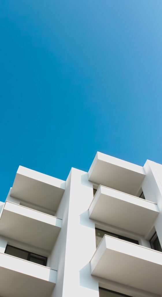 Low-angle view of a modern white apartment building with clean balconies against a clear blue sky, similar in style to Park One, JVT