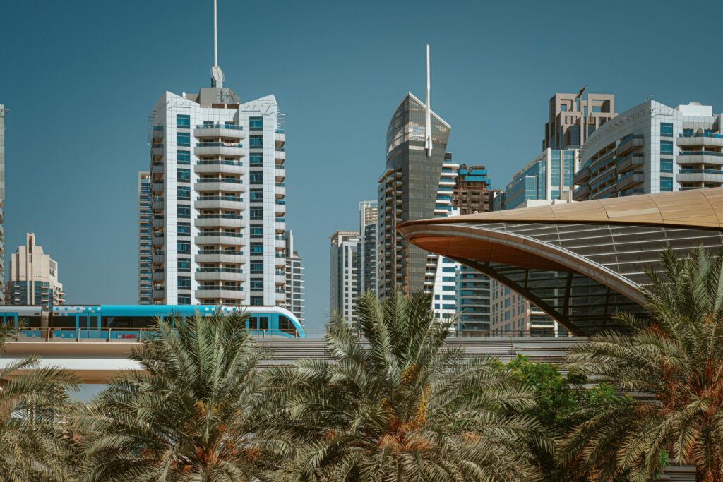 Dubai residential towers behind palm trees and a metro train