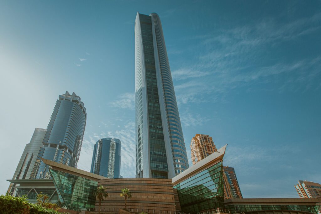 Low-angle view of a modern glass residential tower rising above lower buildings under a clear blue sky in Dubai