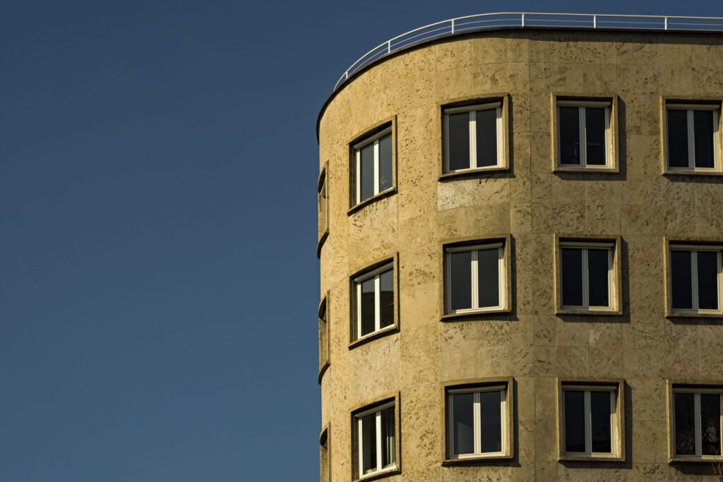 Curved sandstone-toned apartment building facade under a deep blue sky, similar in style to Milestone Residences, JVT