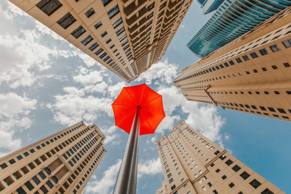 Upward view of Dubai high-rise towers framing a red sculpture against blue sky near Sadaf 4, JBR