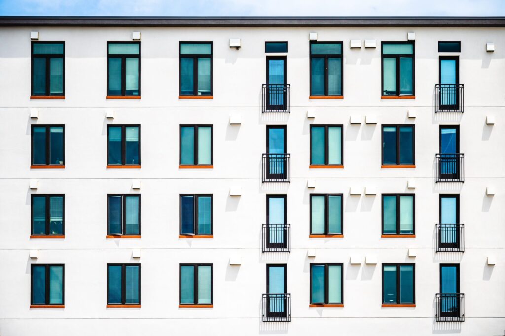 Modern white apartment building facade with dark glass windows and small balconies, similar in style to Emerald Vision Tower, JVT