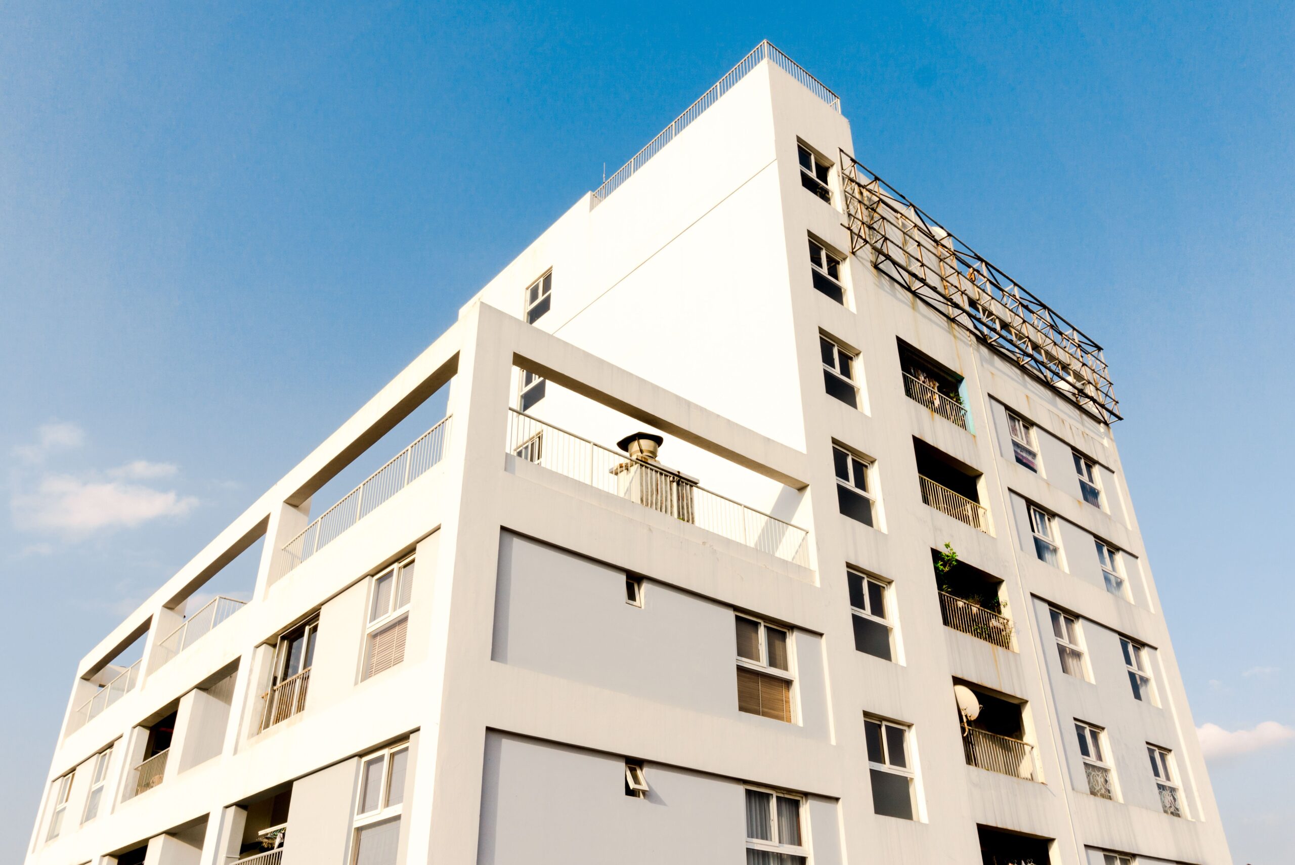 Low angle view of a white modern mid-rise Dubai apartment building with balconies against a clear blue sky