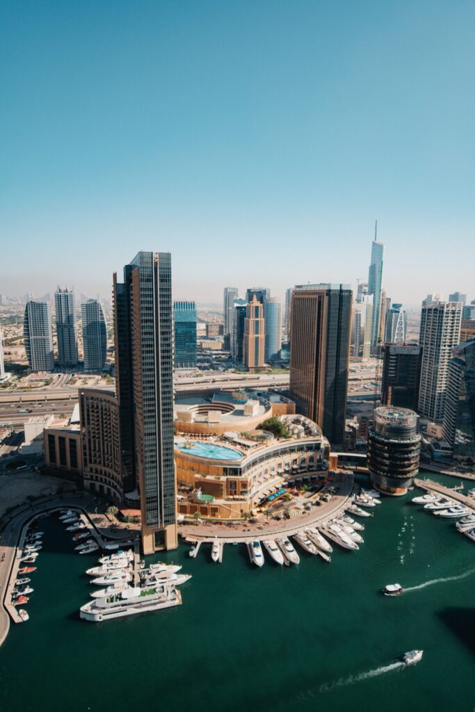 Aerial daytime view of Dubai Marina towers, a rooftop pool deck and a yacht-lined marina waterway