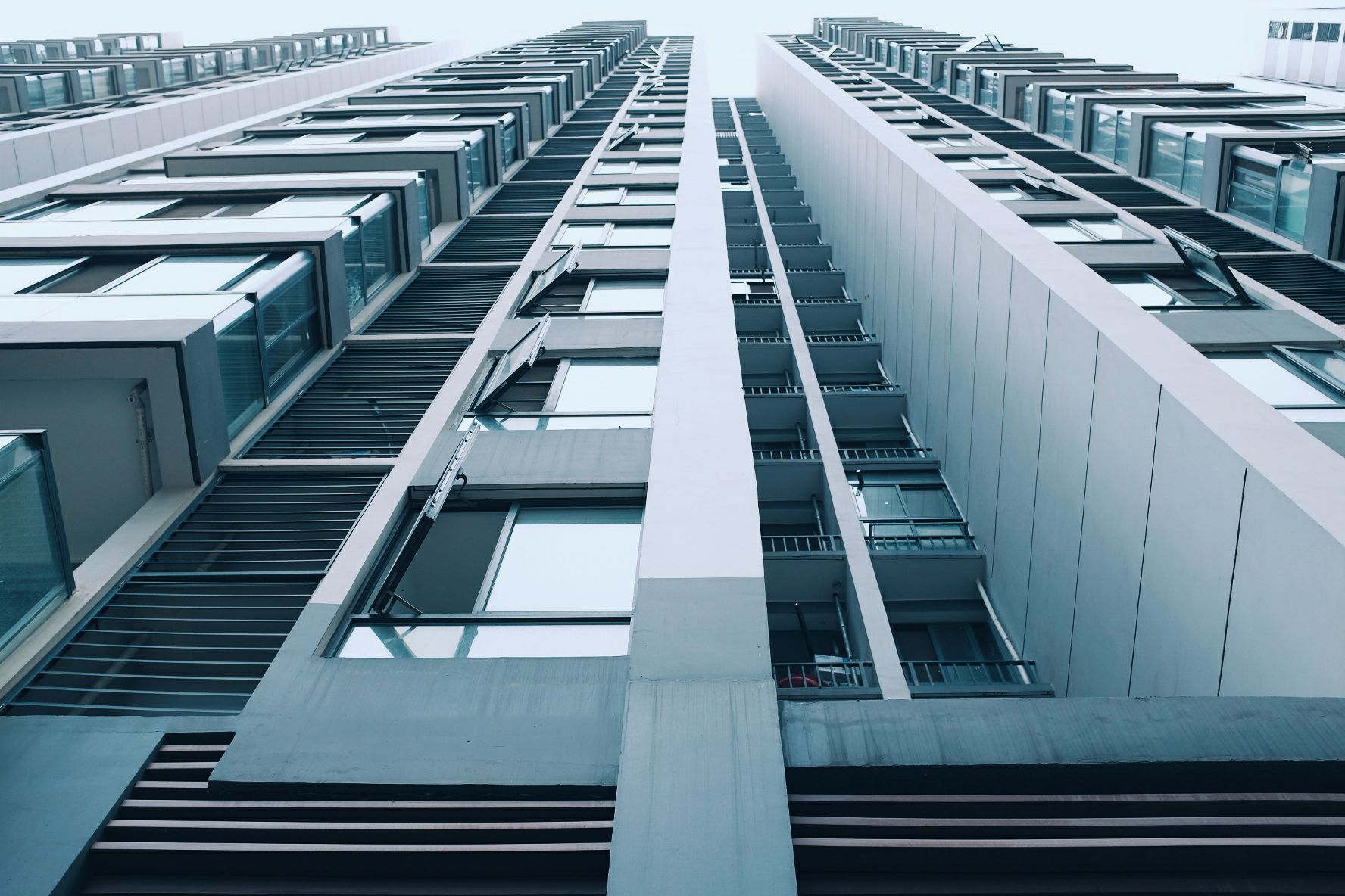Modern apartment tower with recessed balconies seen from below against a pale sky