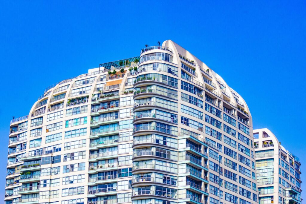 Low angle view of a curved cream modern apartment building corner with a landscaped rooftop terrace against a clear blue sky in Dubai