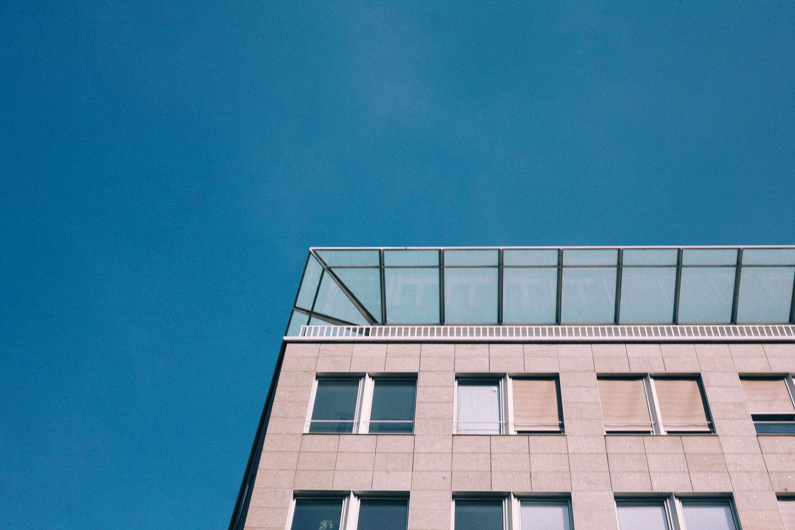 Beige stone-tile modern building corner with a glass rooftop element against a deep blue sky, representative of Monaco Residency in Liwan