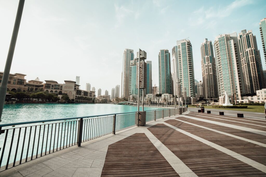 Canal-front boardwalk beside a lake with the Downtown Dubai skyline of high-rise residential towers in the background