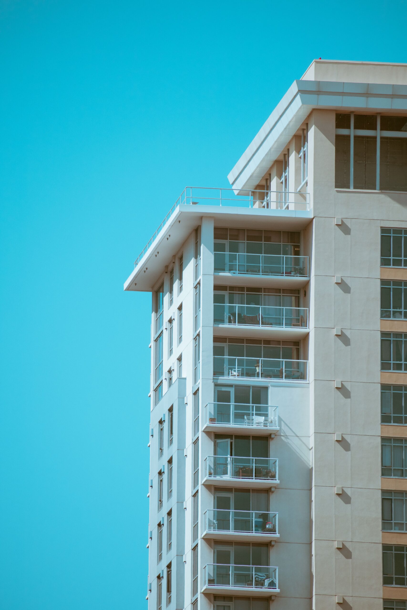 Cream-toned modern residential tower with glass balconies against a clear blue sky, similar in style to Manara Tower, JVT