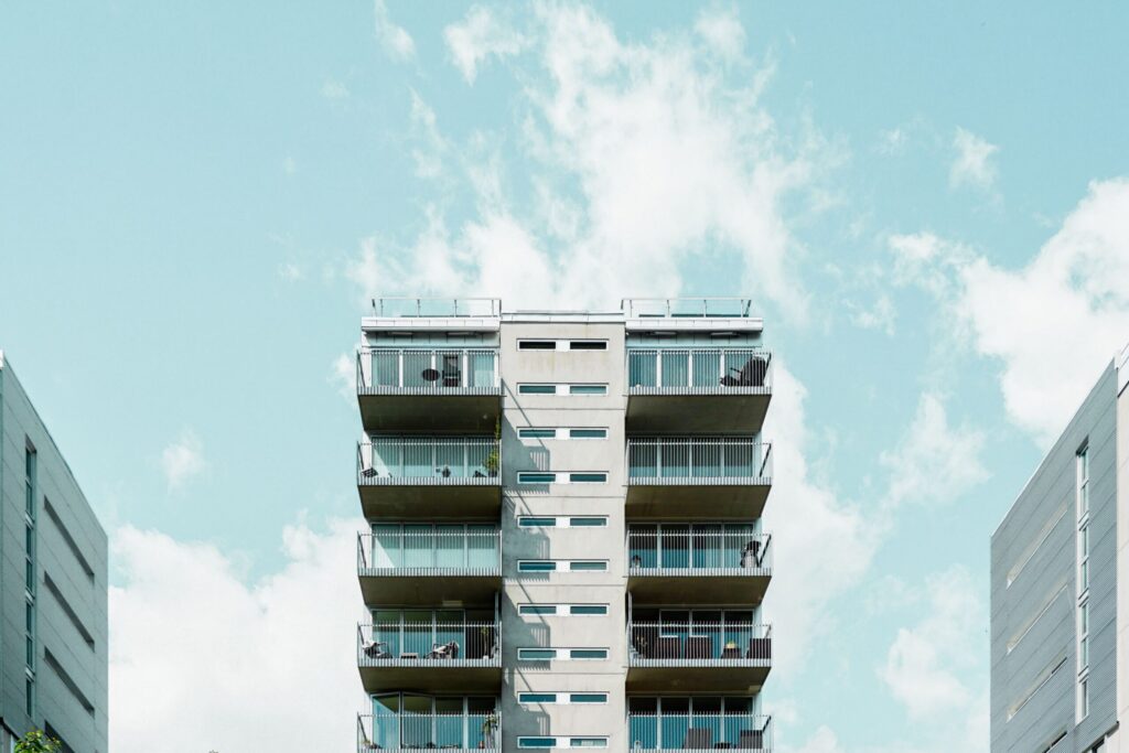 Mid-rise apartment building with balconies rising between two facades under a pale blue sky