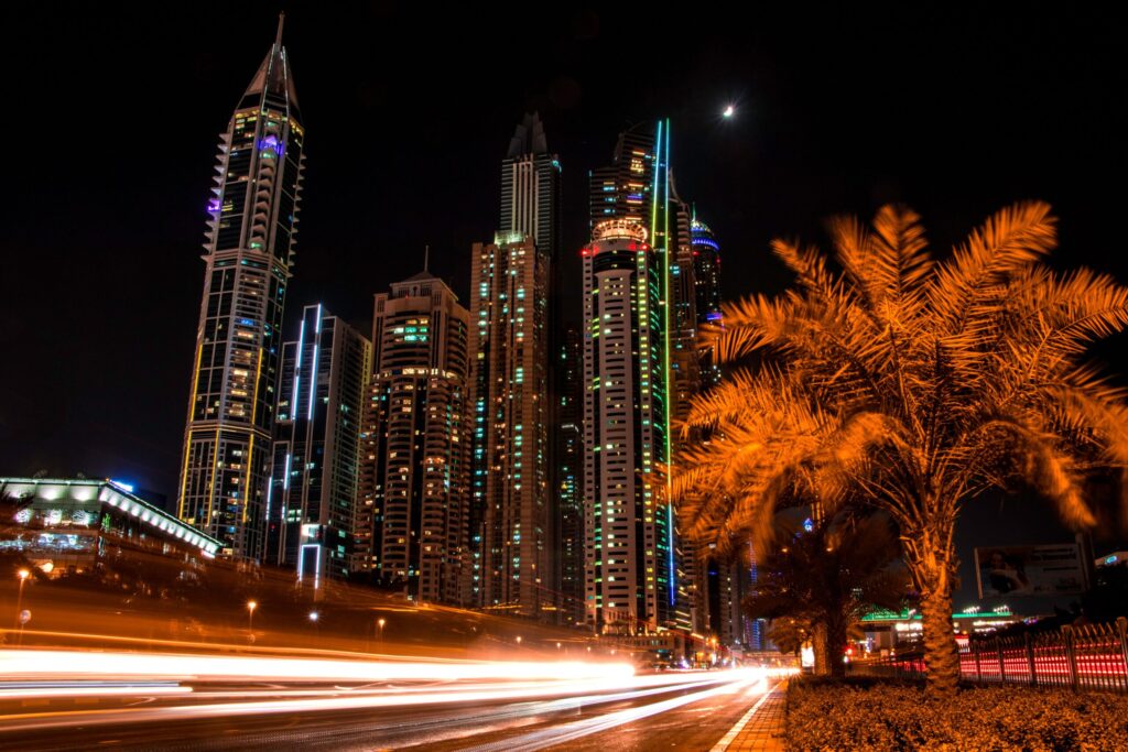 Illuminated Dubai skyline at night with palm trees and light trails from passing traffic, representative of the wider Dubai Production City area near Sol Golf Views