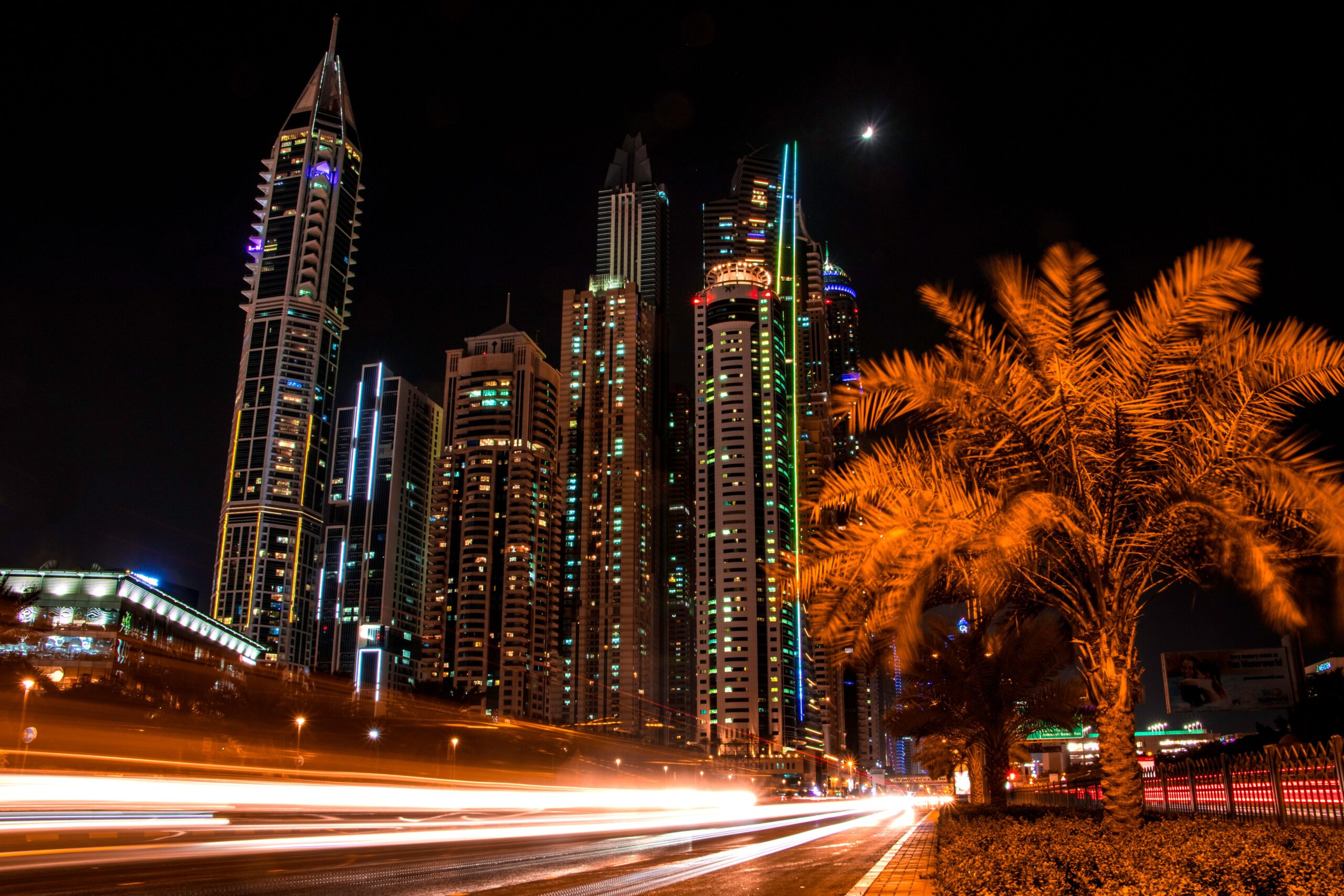Illuminated Dubai skyline at night with palm trees and light trails from passing traffic, representative of the wider Dubai Production City area near Sol Golf Views