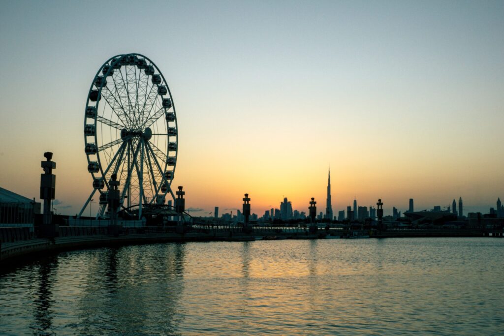 Ferris wheel silhouetted against a golden sunset with the Dubai skyline behind