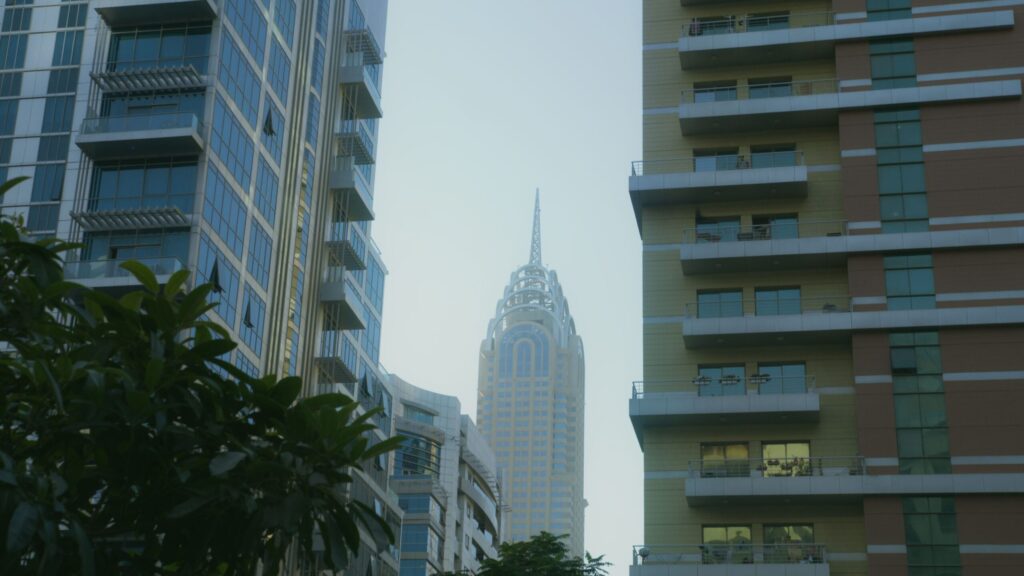 Dubai apartment towers framing a distant spired skyscraper under a hazy sky, representative of The Pulse Residence in Dubai South, Dubai