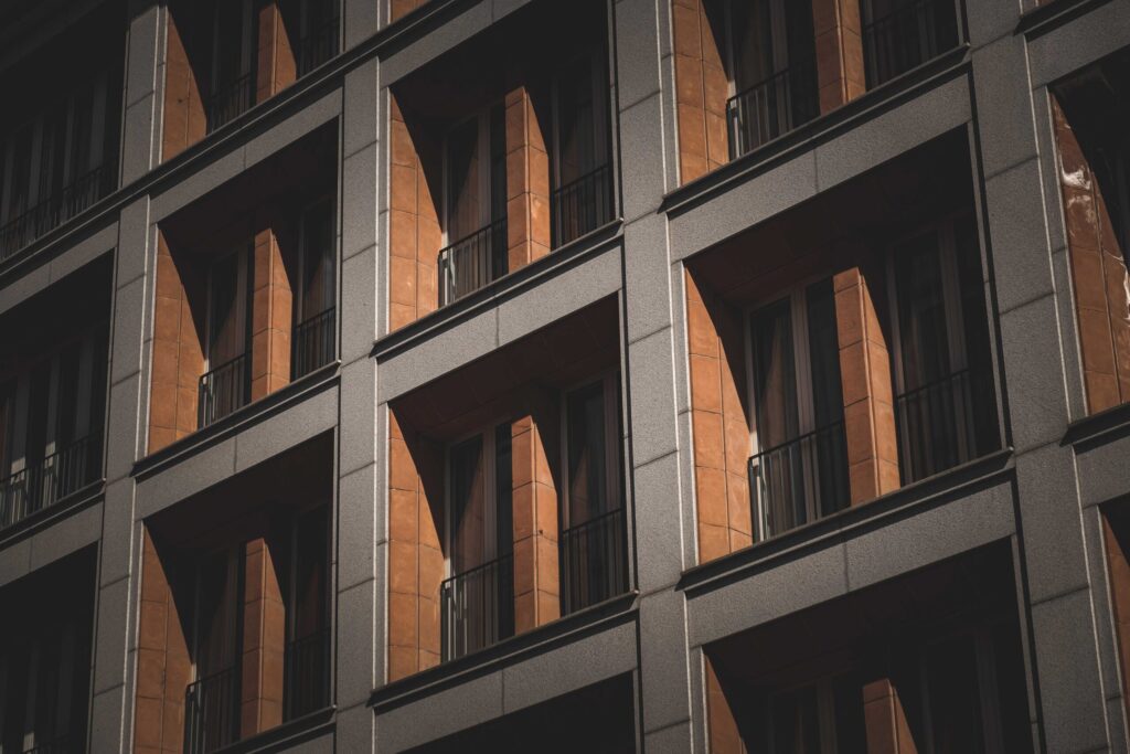 Close angled view of a modern apartment building facade with terracotta-accented balconies and grey concrete framing under natural light, representative of contemporary residential architecture near Azizi Tulip in Al Furjan, Dubai