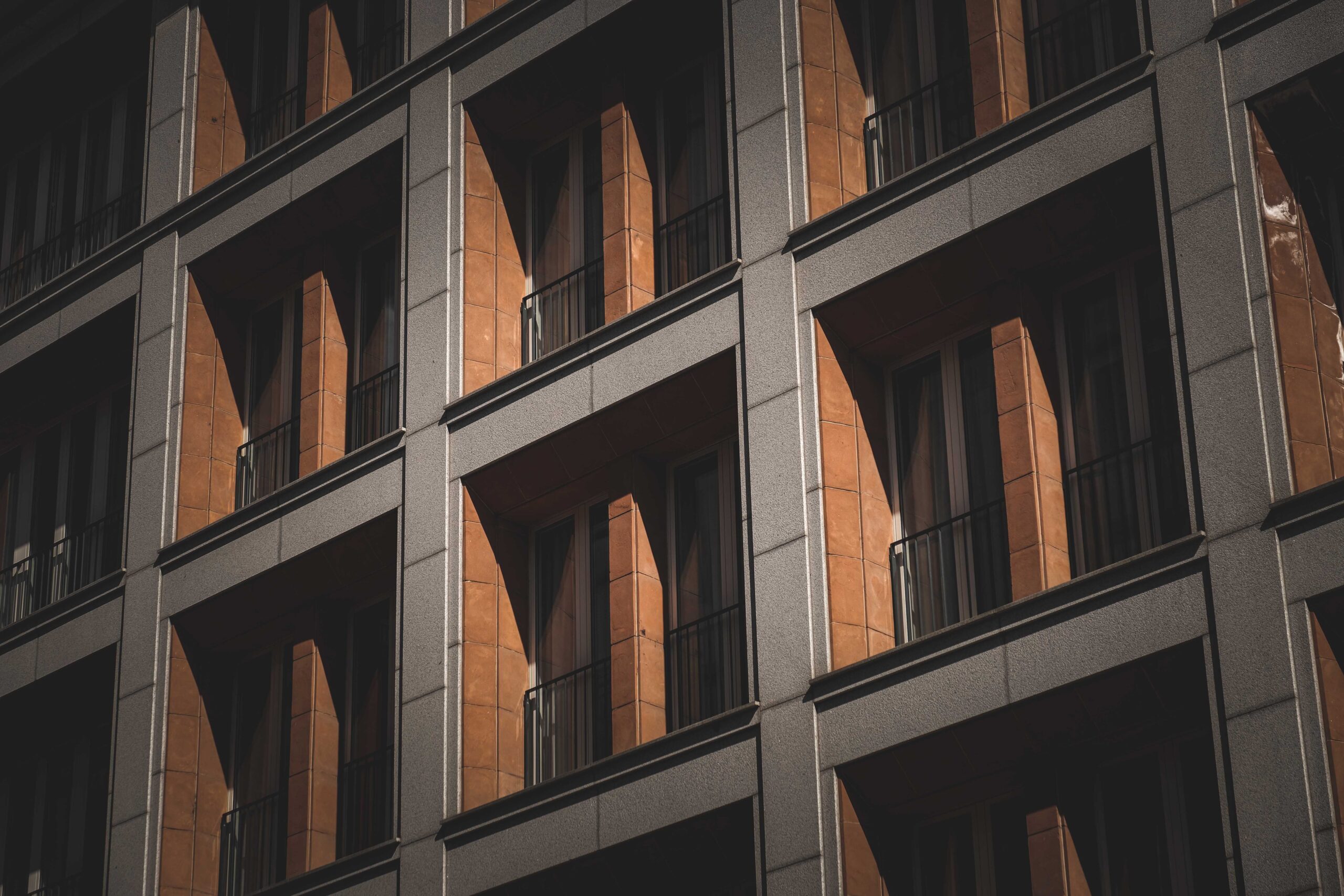 Close angled view of a modern apartment building facade with terracotta-accented balconies and grey concrete framing under natural light, representative of contemporary residential architecture near Azizi Tulip in Al Furjan, Dubai