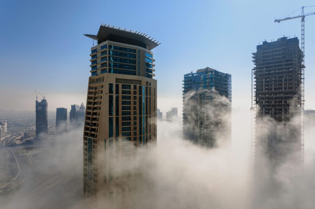 Dubai skyscrapers emerging from morning fog with a crane on a tower under construction