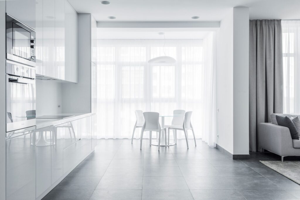 Bright modern white kitchen and dining area with sheer curtains and floor-to-ceiling windows in a Dubai apartment