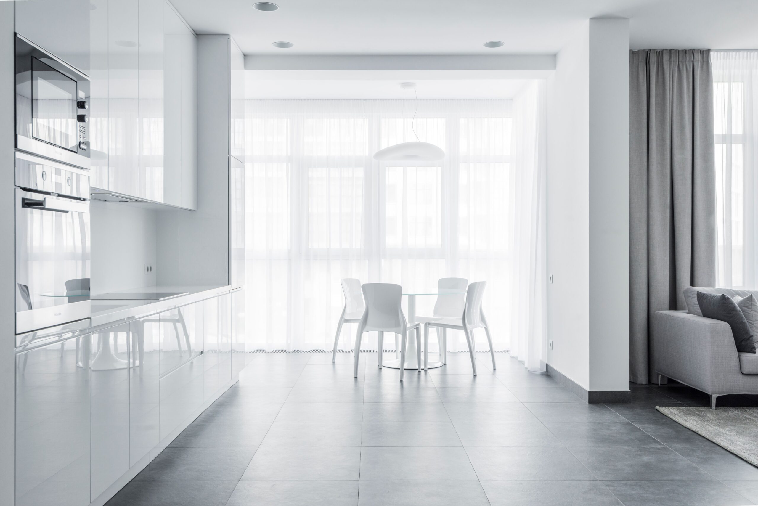 Bright modern white kitchen and dining area with sheer curtains and floor-to-ceiling windows in a Dubai apartment
