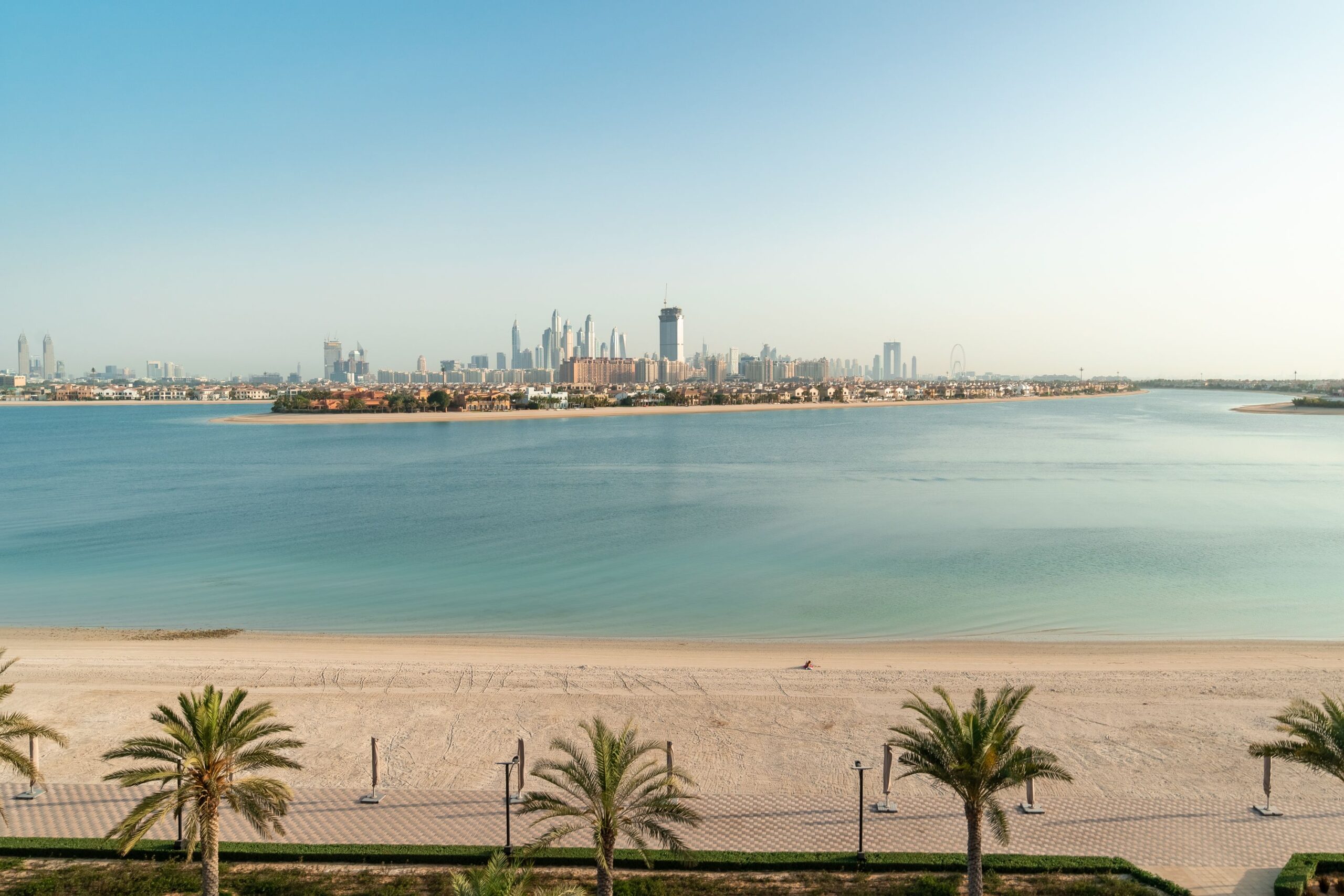 Palm-lined beach promenade on Palm Jumeirah with the Dubai skyline in the distance, near the planned Sol Beach development