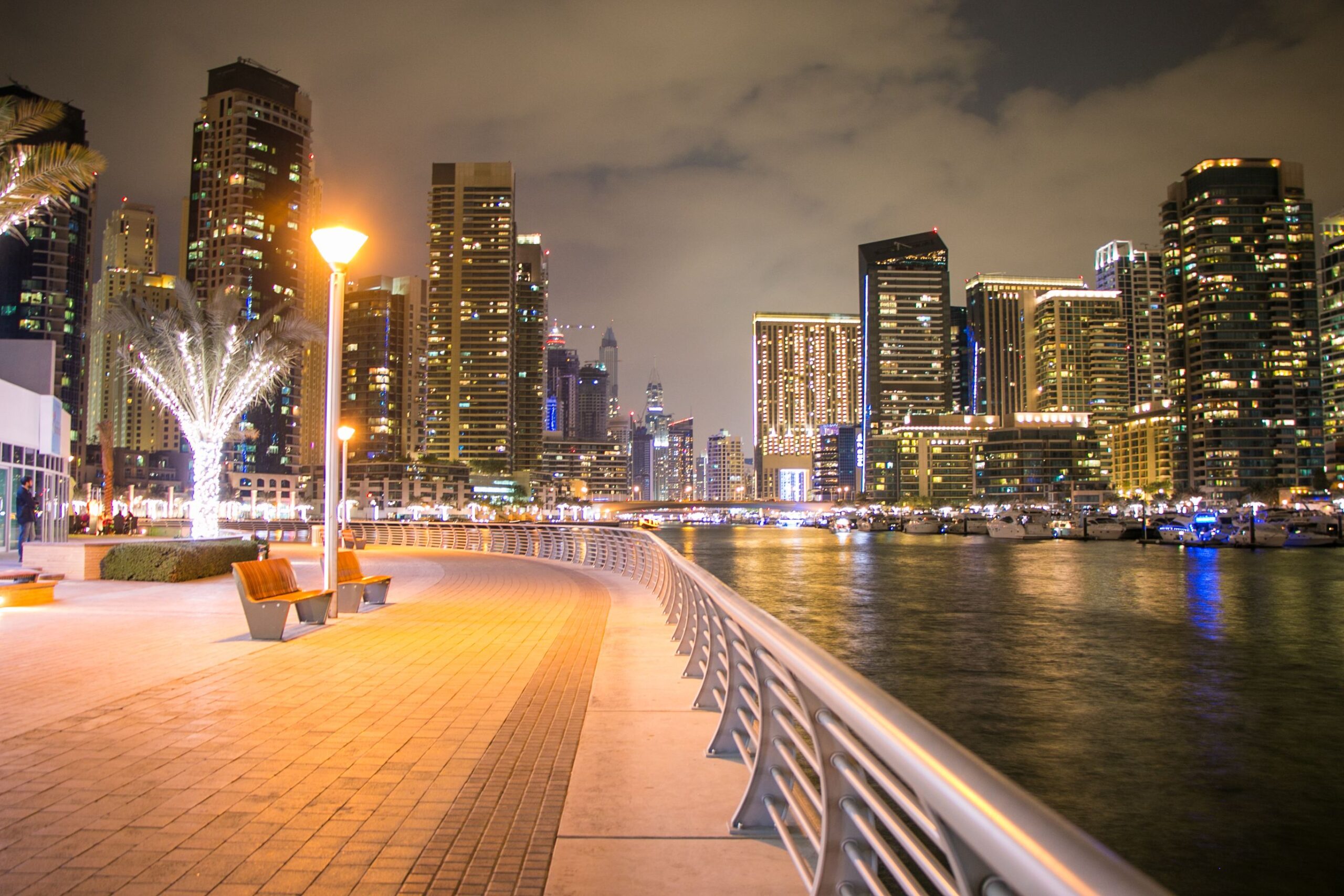 Dubai Marina promenade at night with an illuminated tower skyline and yacht marina reflections across the water