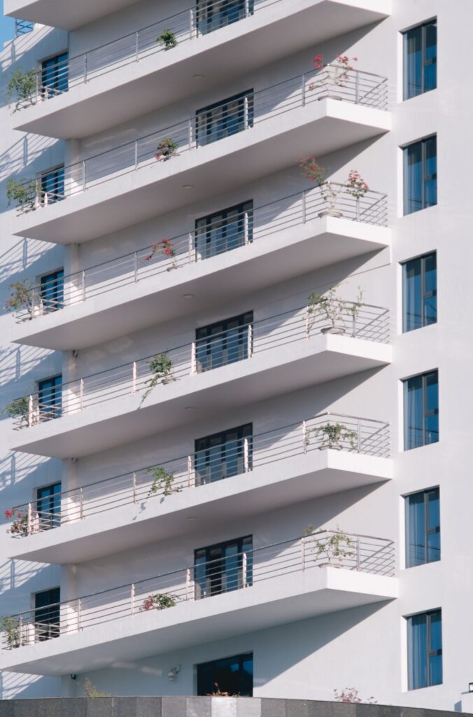Clean white modern apartment building with staggered balconies and blue-tinted windows under a clear sky, evocative of a Liwan, Dubai residential development