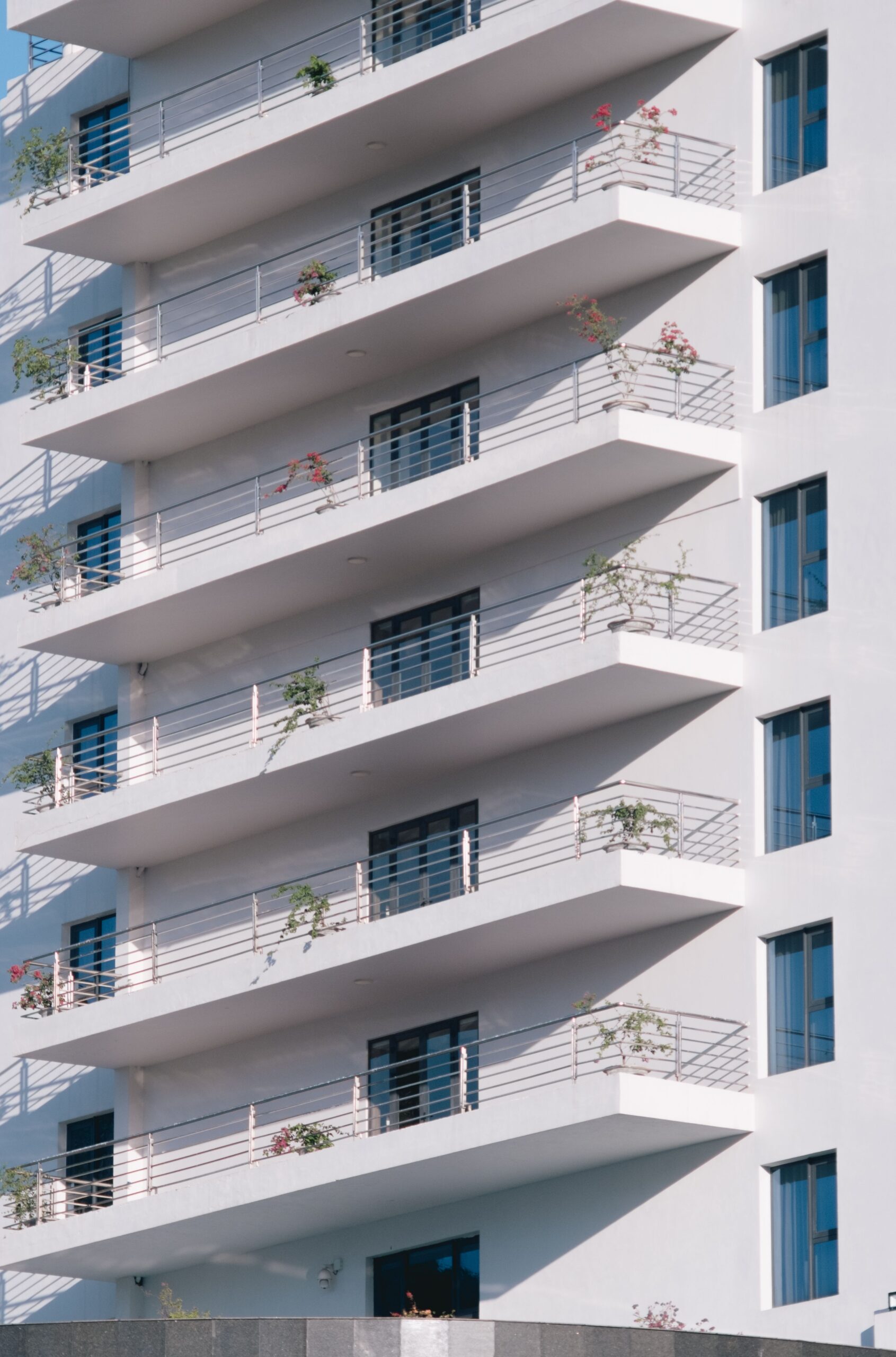 Clean white modern apartment building with staggered balconies and blue-tinted windows under a clear sky, evocative of a Liwan, Dubai residential development