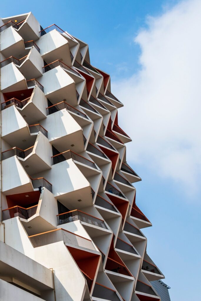White triangular geometric balcony facade with terracotta accents against a clear blue sky, representative of National Bonds Jewels in Liwan