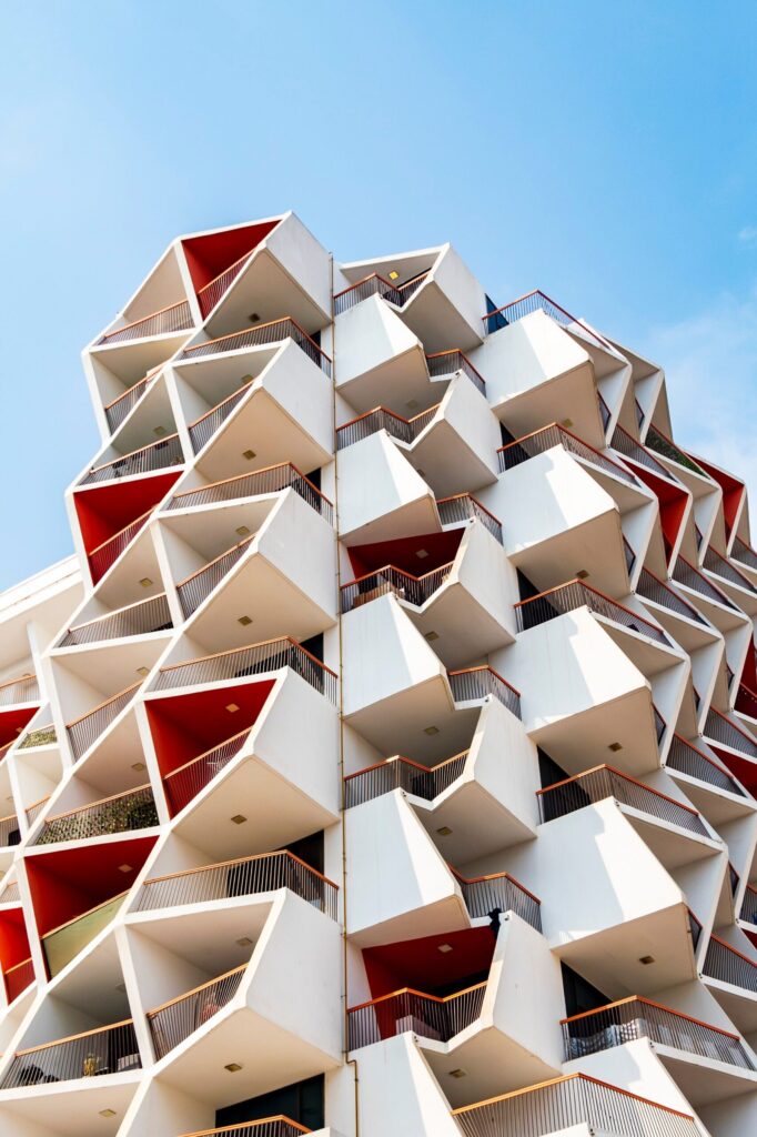 Modern Dubai residential building facade with geometric red and white triangular balconies against a clear blue sky, representative of contemporary architecture in Dubai Creek Harbour where Rosewater at Creek Beach is located