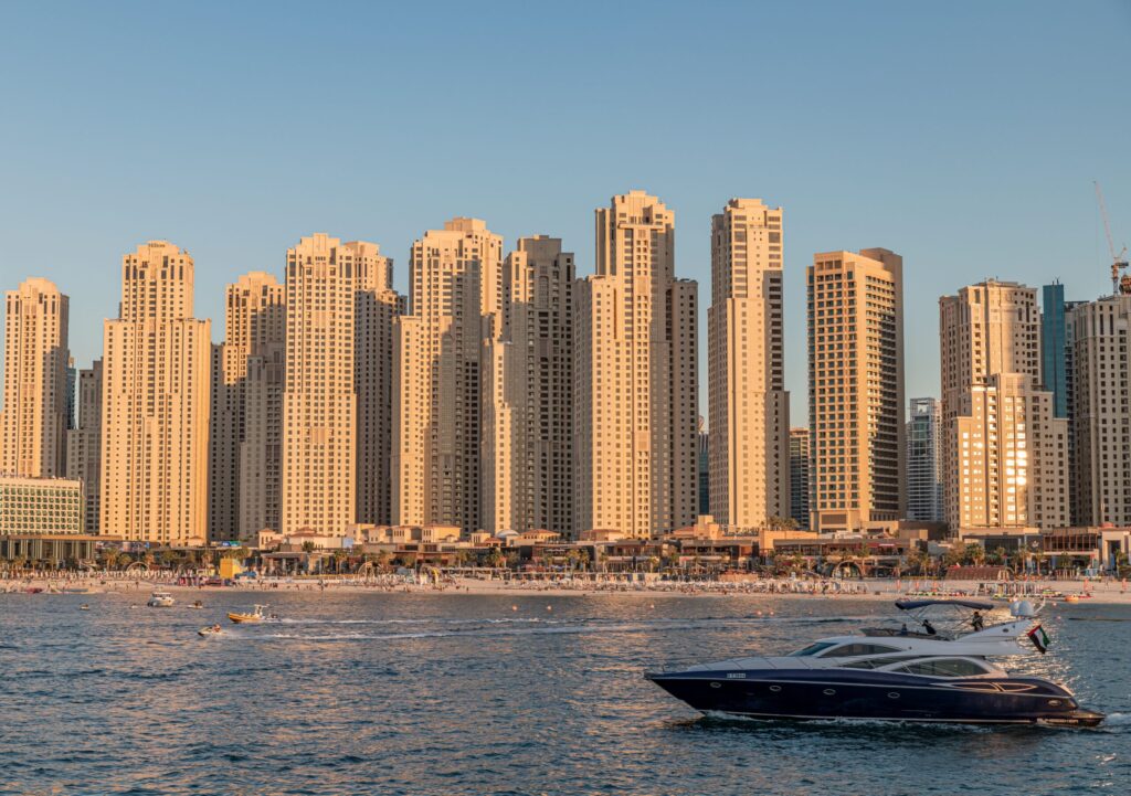 Golden-hour view of the Jumeirah Beach Residence (JBR) beachfront tower skyline from the water, with a motor yacht passing in the foreground, Dubai
