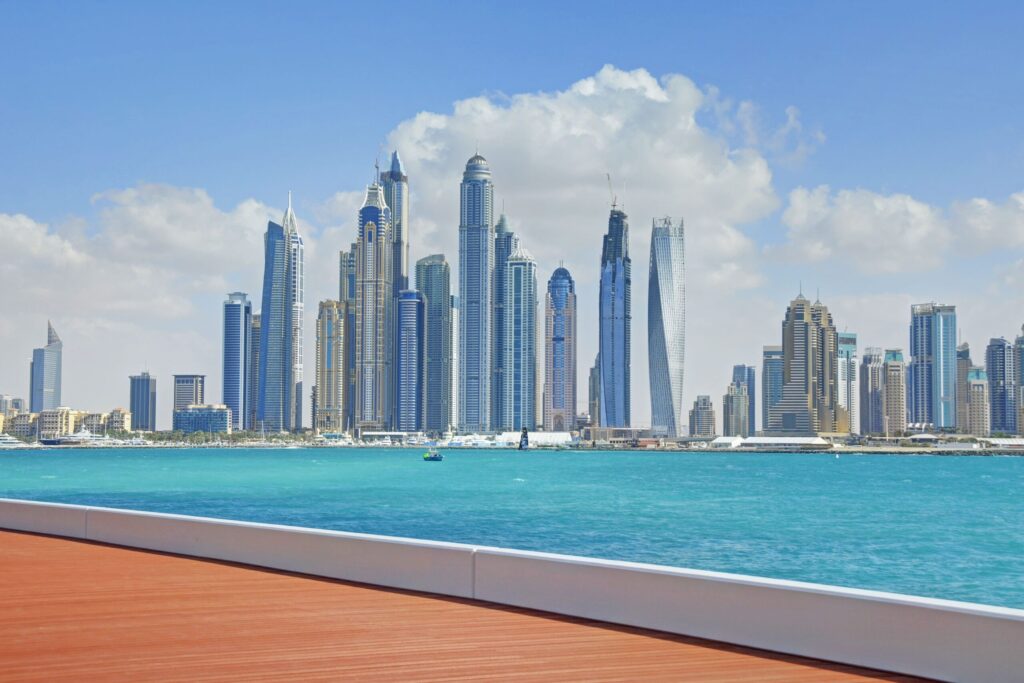 Vivid turquoise-water promenade view of the Dubai Marina skyline with the Cayan Tower's twisted silhouette, near Al Seef Tower