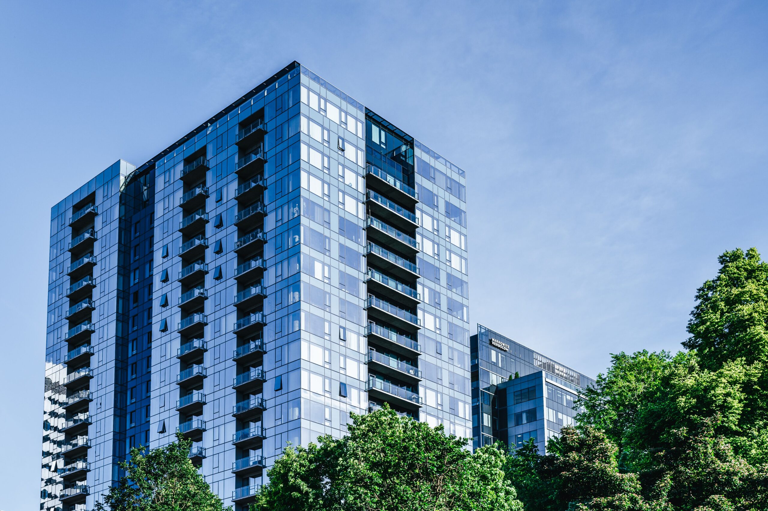 Low-angle view of a modern glass-facade high-rise apartment building with balconies and greenery, representative of contemporary Dubai Hills Estate architecture