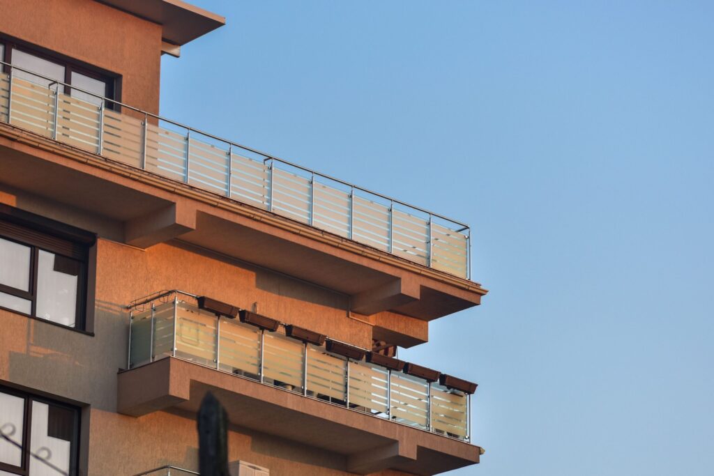 Corner of a modern terracotta-coloured low-rise apartment building with frosted glass balcony railings against a clear blue sky in Dubai